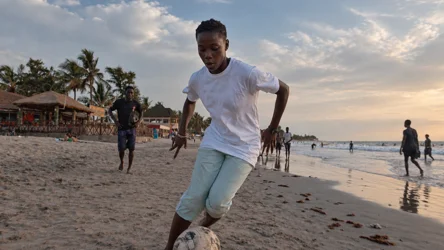 A young player running with the ball on the beach in The Gambia